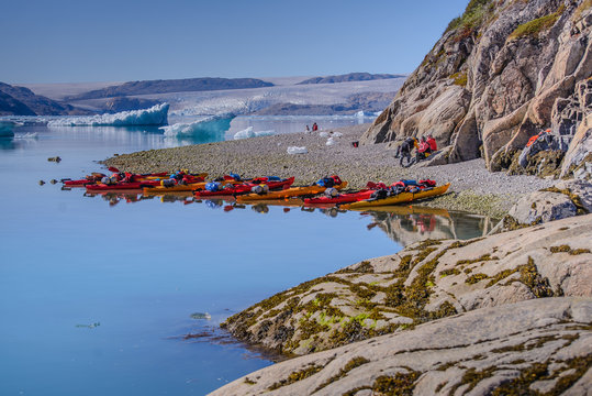 Adventure tourists on fjord beach with rows of kayaks, Narsaq, Vestgronland, South Greenland