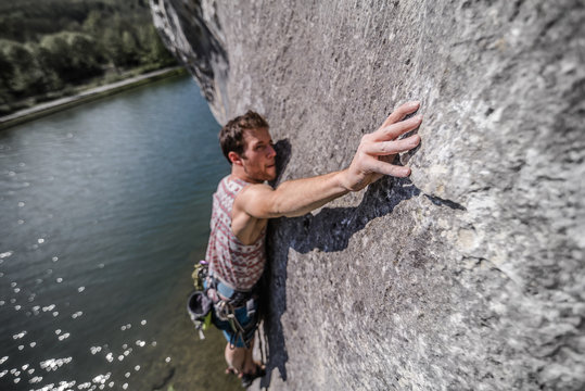 Young male rock climber reaching while climbing limestone rock face, Freyr, Belgium, elevated view