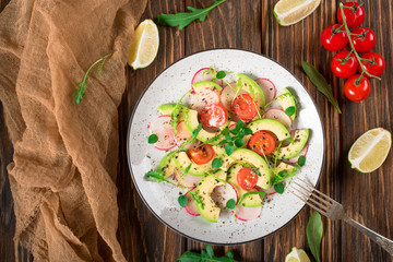 Vegetable salad with avocado, arugula, radish, lime and olive oil. Dietary healthy food. Wooden rustic background. Top view