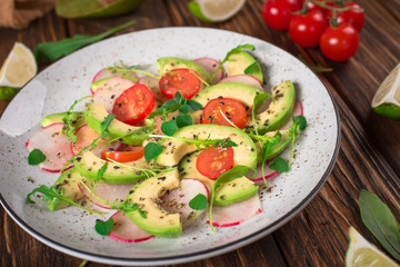 Vegetable salad with avocado, arugula, radish, lime and olive oil. Dietary healthy food. Wooden rustic background. Top view