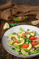 Vegetable salad with avocado, arugula, radish, lime and olive oil. Dietary healthy food. Wooden rustic background. Top view
