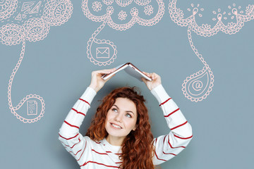 Cheerful student. Emotional cheerful student putting her book over the head and smiling