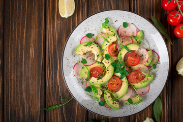 Vegetable salad with avocado, arugula, radish, lime and olive oil. Dietary healthy food. Wooden rustic background. Top view
