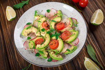 Vegetable salad with avocado, arugula, radish, lime and olive oil. Dietary healthy food. Wooden rustic background. Top view