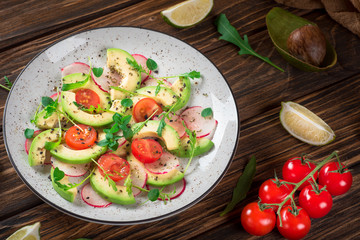 Vegetable salad with avocado, arugula, radish, lime and olive oil. Dietary healthy food. Wooden rustic background. Top view