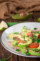Vegetable salad with avocado, arugula, radish, lime and olive oil. Dietary healthy food. Wooden rustic background. Top view