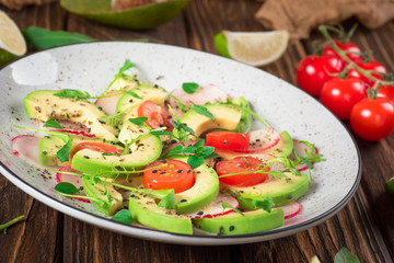 Vegetable salad with avocado, arugula, radish, lime and olive oil. Dietary healthy food. Wooden rustic background. Top view