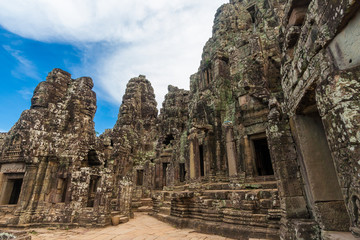 Great view of the third level enclosure of Cambodia's popular Bayon temple under a blue sky. On the right stands the central sanctuary of the temple surrounded by towers with ancient face sculptures.