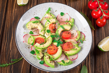 Vegetable salad with avocado, arugula, radish, lime and olive oil. Dietary healthy food. Wooden rustic background. Top view