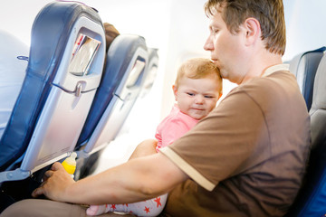 Obraz premium Young tired father and his crying baby daughter during flight on airplane going on vacations