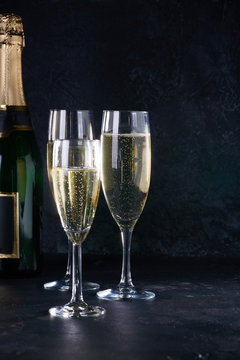 Elegant glasses of yellow champagne with bubbles on black background with reflection