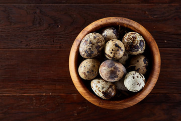 Fresh quail eggs in a wooden bowl on a dark wooden background, top view, close-up