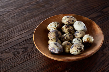Fresh quail eggs in a wooden plate on a dark wooden background, top view, close-up