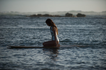 Girl sits meditatively on her surfboard