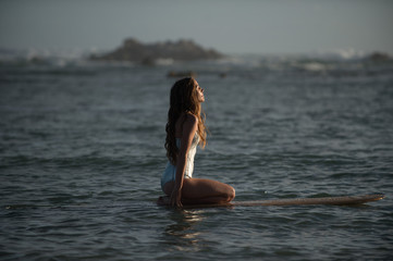 Girl closes her eyes in the evening light while sitting on her surfboard