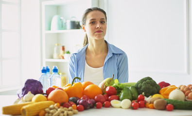 happy young housewife sitting in the kitchen preparing food from a pile of diverse fresh organic fruits and vegetables