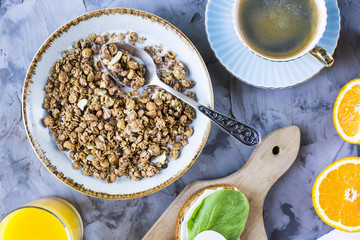 Healthy hearty breakfast - muesli, sandwich with egg, coffee, orange and juice on a gray background. Top view