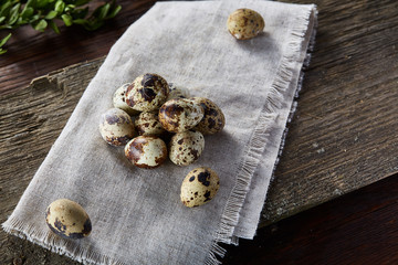 Quail eggs arranged in pyramid on a napkin with boxwood branches over a wooden table, close-up, selective focus.