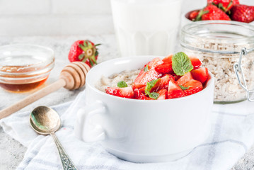 Healthy summer breakfast, overnight oatmeal with fresh strawberry and milk, grey stone background