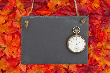 Autumn time with a chalkboard with retro pocket watch and fall leaves