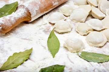 Dumplings with meat, rolling pin, flour, bay leaf on the table close-up.