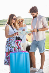 Naklejka premium Young man showing directions on the map to two beautiful young female tourists. Standing in front of the airport terminal building with suitcases, maps, passports and camera.