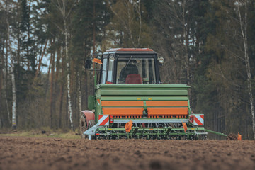 Land being cultivated and prepared for sowing with a tractor. Crispy texture in the soil. Old russian tractor with modern sow machine attached. Wheel, gauges and cabin.