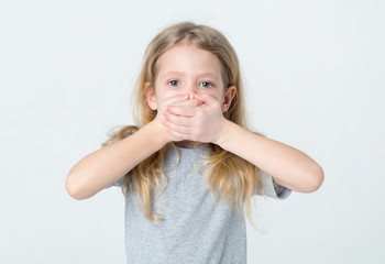 Silent, do not talk. Little girl covered her mouth with her hands on a light background.