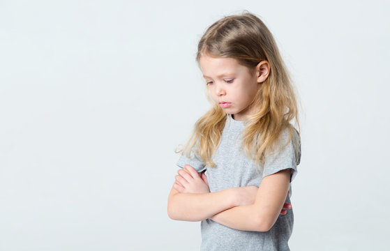 Sad little girl standing on a light background.