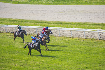 Galloping race horses and jockeys in racing competition