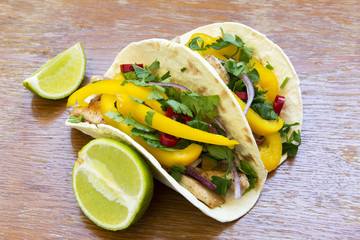 Mexican tacos with grilled chicken fillet, fresh vegetables and lime on rustic wooden background. Side view, closeup.