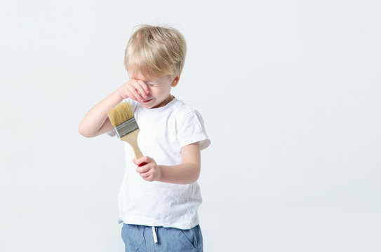 Crying little boy is holding a paintbrush in his hands. He cries and wants to paint.
