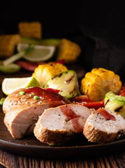 Chicken fillet with sauce and grilled vegetables on a wooden background.