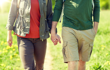 travel, hiking, backpacking, tourism and people concept - close up of couple with backpacks holding hands and walking along country road