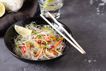Vietnamese Pho Noodle Soup. Chilli, Rice Noodles, Bean Shoots showing noodles picked up with Chopsticks on a black background.