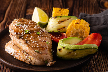 Chicken fillet with sauce and grilled vegetables on a wooden background.