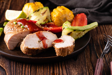 Chicken fillet with sauce and grilled vegetables on a wooden background.