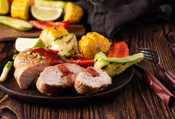 Chicken fillet with sauce and grilled vegetables on a wooden background.