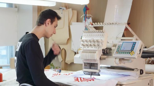 Young man is embroidering pattern on computerized machine