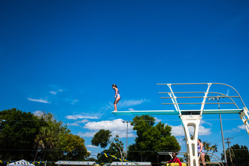A girl jumping off of a diving board up high blue sky