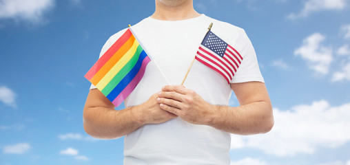 lgbt, same-sex relationships and homosexual concept - close up of man holding gay pride rainbow and american flag over blue sky and clouds background