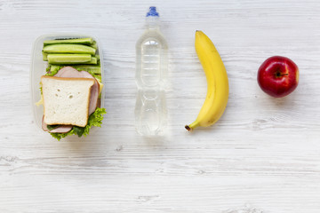 Healthy school lunch box with sandwich, fruits and bottle of water on white wooden background, top view. From above.