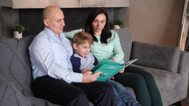 Father, mother and son are reading a book sitting on the sofa