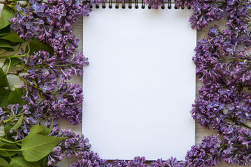 A bouquet of lilac flowers with notebook on a white wooden background. Mothers Day. Copy space. From above, flat lay.