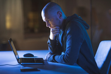 cybercrime, hacking and technology crime - male hacker in dark room with laptop computer