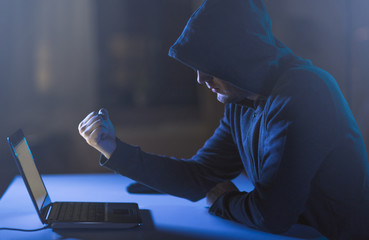 cybercrime, hacking and technology crime - male hacker showing fist to laptop computer in dark room