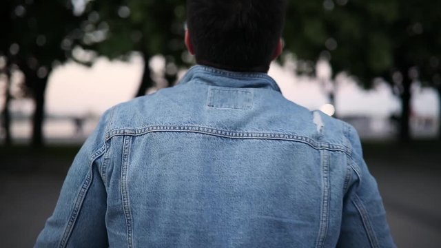 Back of man in torn jeans jacket walking in city park