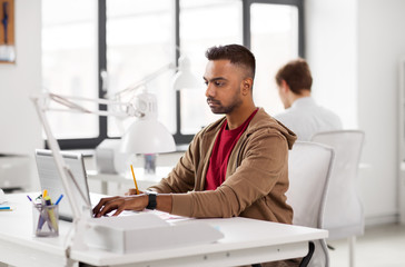 business and creative people concept - young indian man with laptop computer working at office