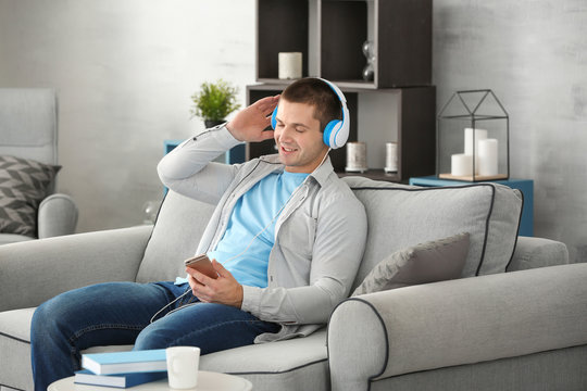Young man listening to music through headphones on sofa at home