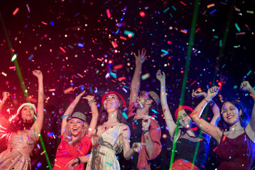 In selective focus of Cheerful young people showered with throwing confetti on a club party.Festival Event Party with People concept.Clubber drinking.